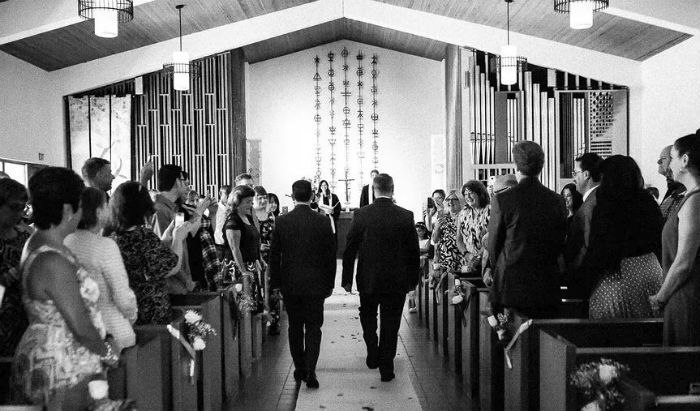 A photo of two men walking down the aisle toward the altar, with the pews full of guests.