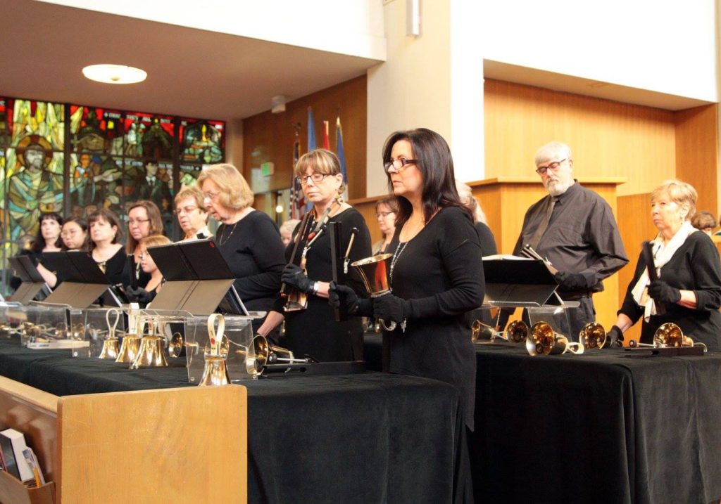 A group of people dressed in all black, playing hand bells.