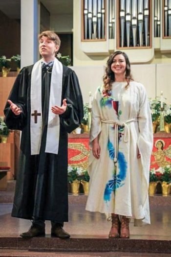 Pastors Jen and Jacob, wearing robes, smiling, and addressing the congregation