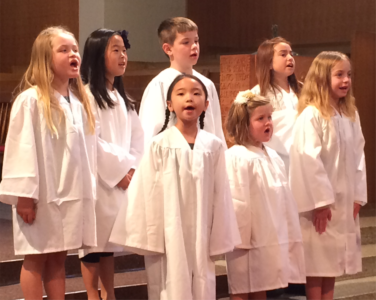 A group of young children wearing white robes and singing.