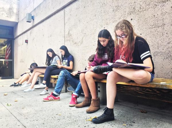 A group of youth, sitting on a bench and writing in their binders.