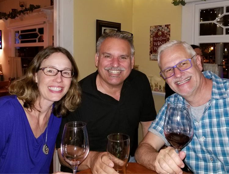 Three smiling adults, holding wine glasses and looking at the camera