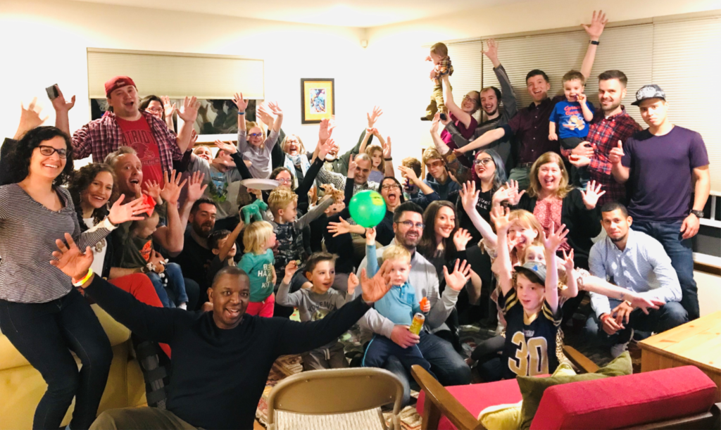 A large group of young adults and children, smiling and waving at the camera