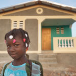 A young girl smiles at the camera, standing in front of a newly built house