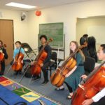Five people, seated, all holding cellos and bows