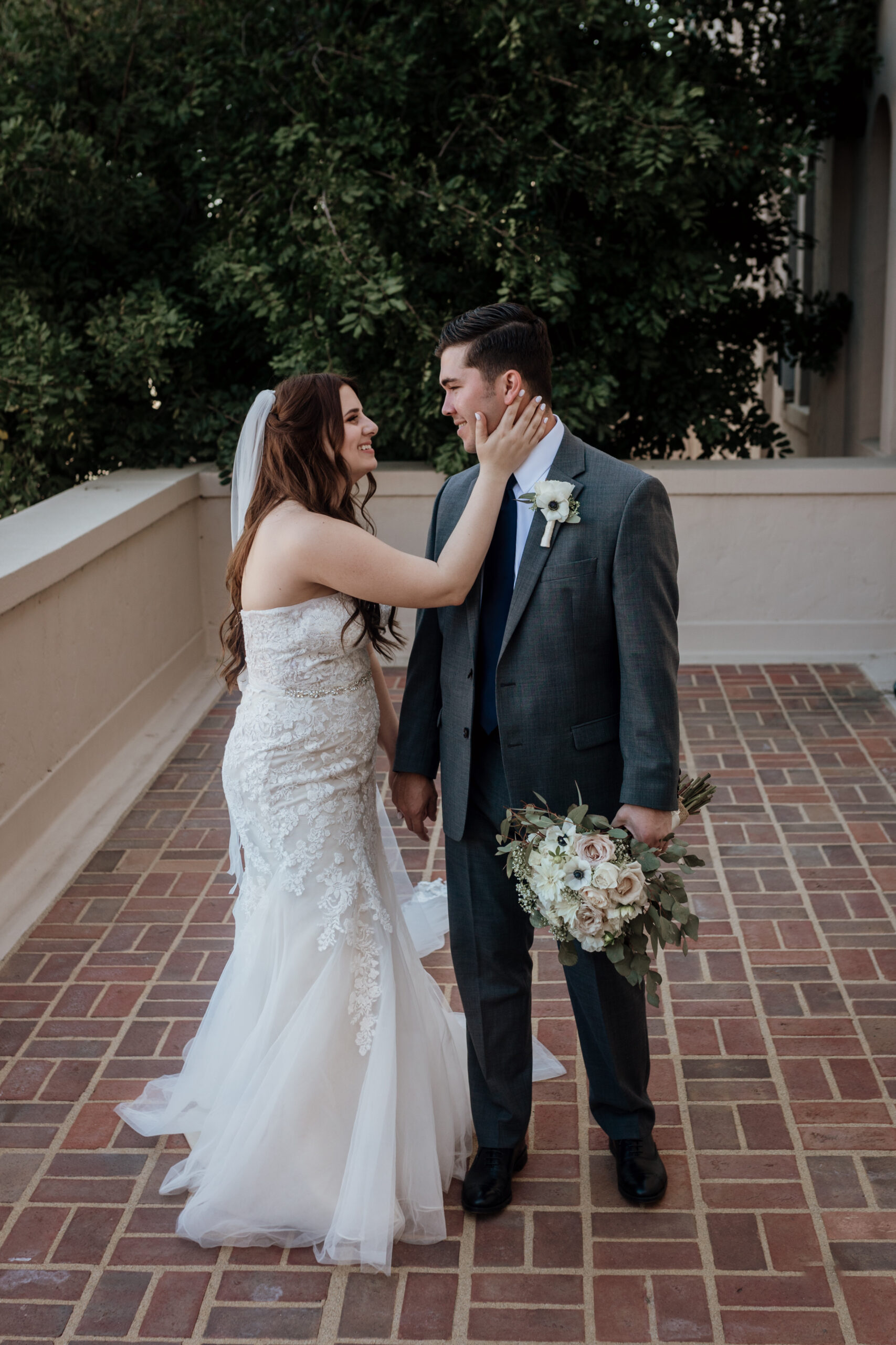 A bride and groom smiling at each other with her hand on his cheek.