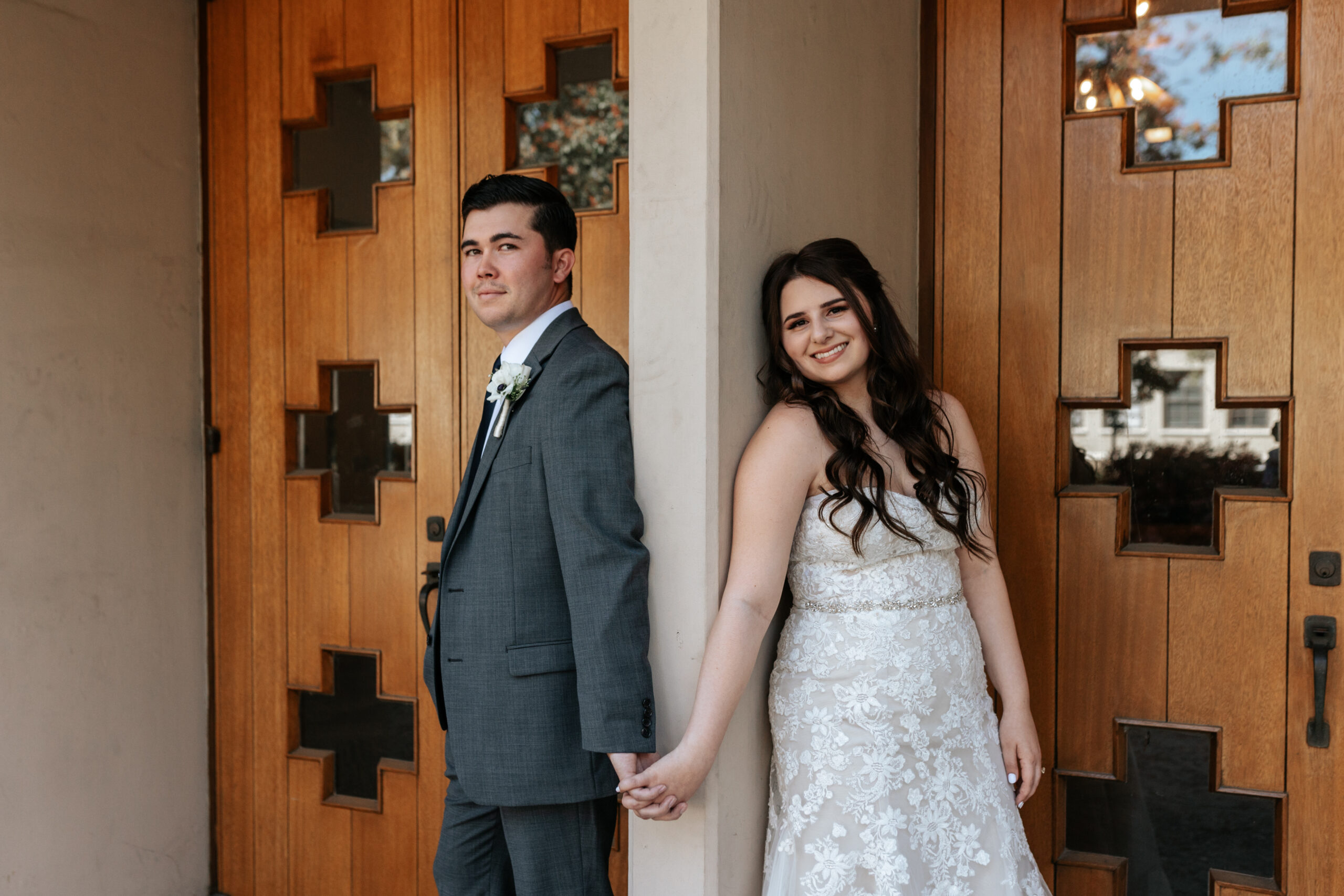 A bride and groom smiling at the camera, holding hands in front of the decorative doors of the Sanctuary.