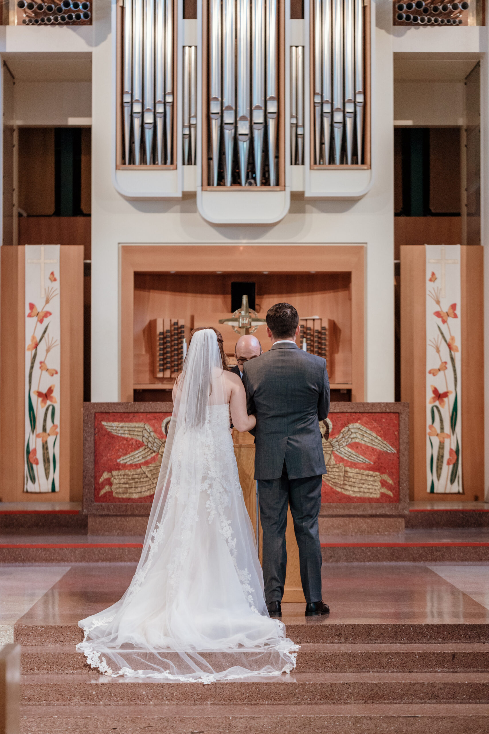 A bride and groom standing at the altar, in front of a huge pipe organ
