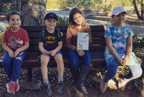 Four kids sitting on a park bench and smiling at the camera