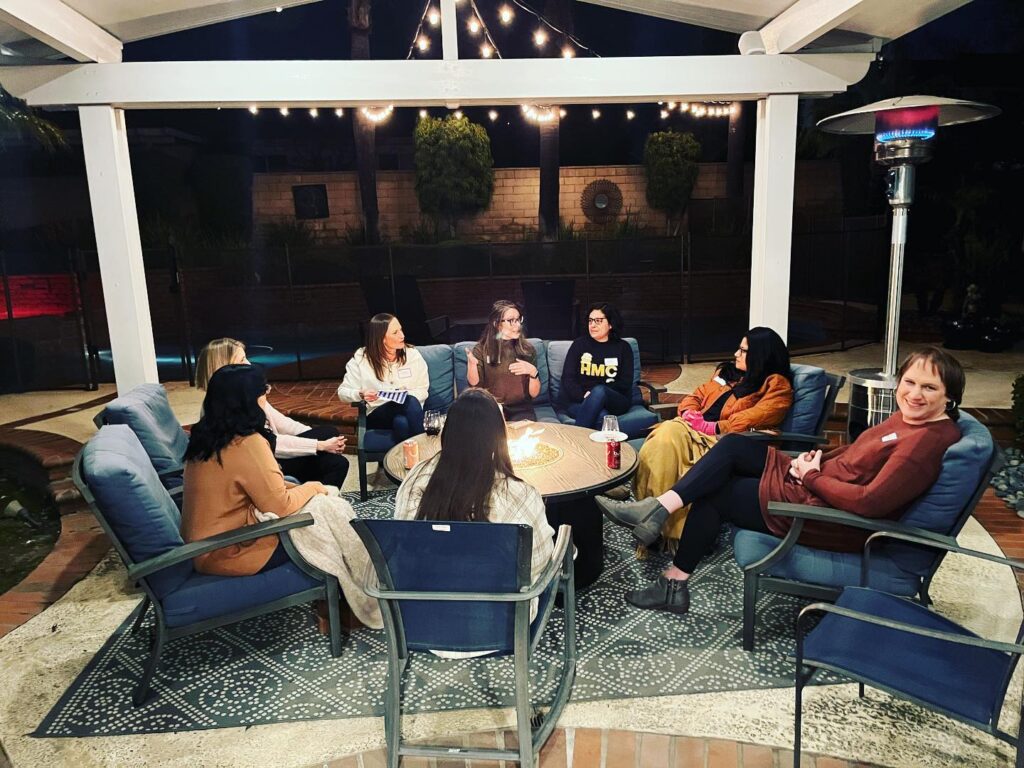 A group of women in their 30's-40's talking around a fire in someone's backyard